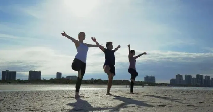 Three people doing yoga on the beach.
